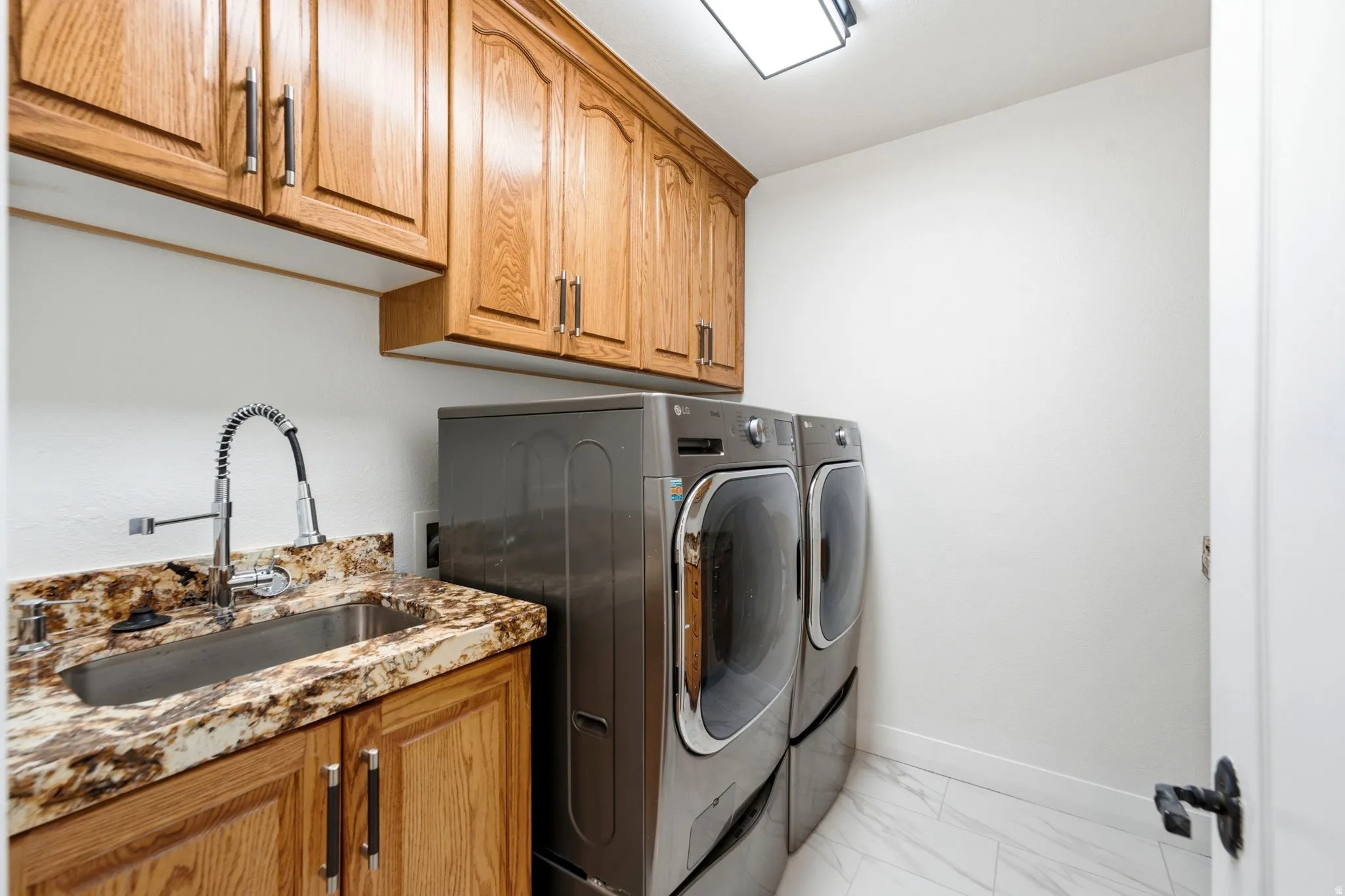 Laundry area featuring wood cabinetry, stainless steel sink, patterned countertop, and white tile flooring