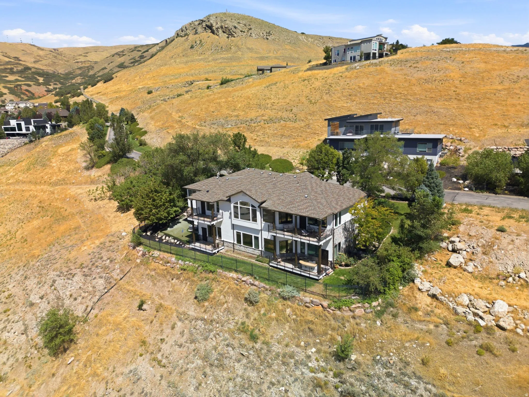 Two-story residence featuring a gabled roof, multiple balconies, a fenced yard, and surrounding mountainous terrain