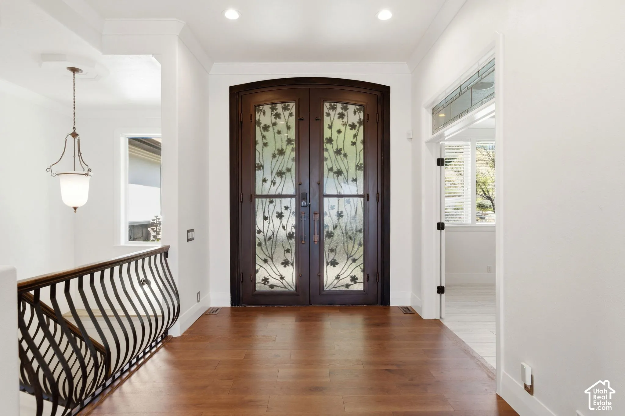 Arched entryway doors with decorative glass panels, wood-finish flooring, wrought iron railing, and recessed lighting
