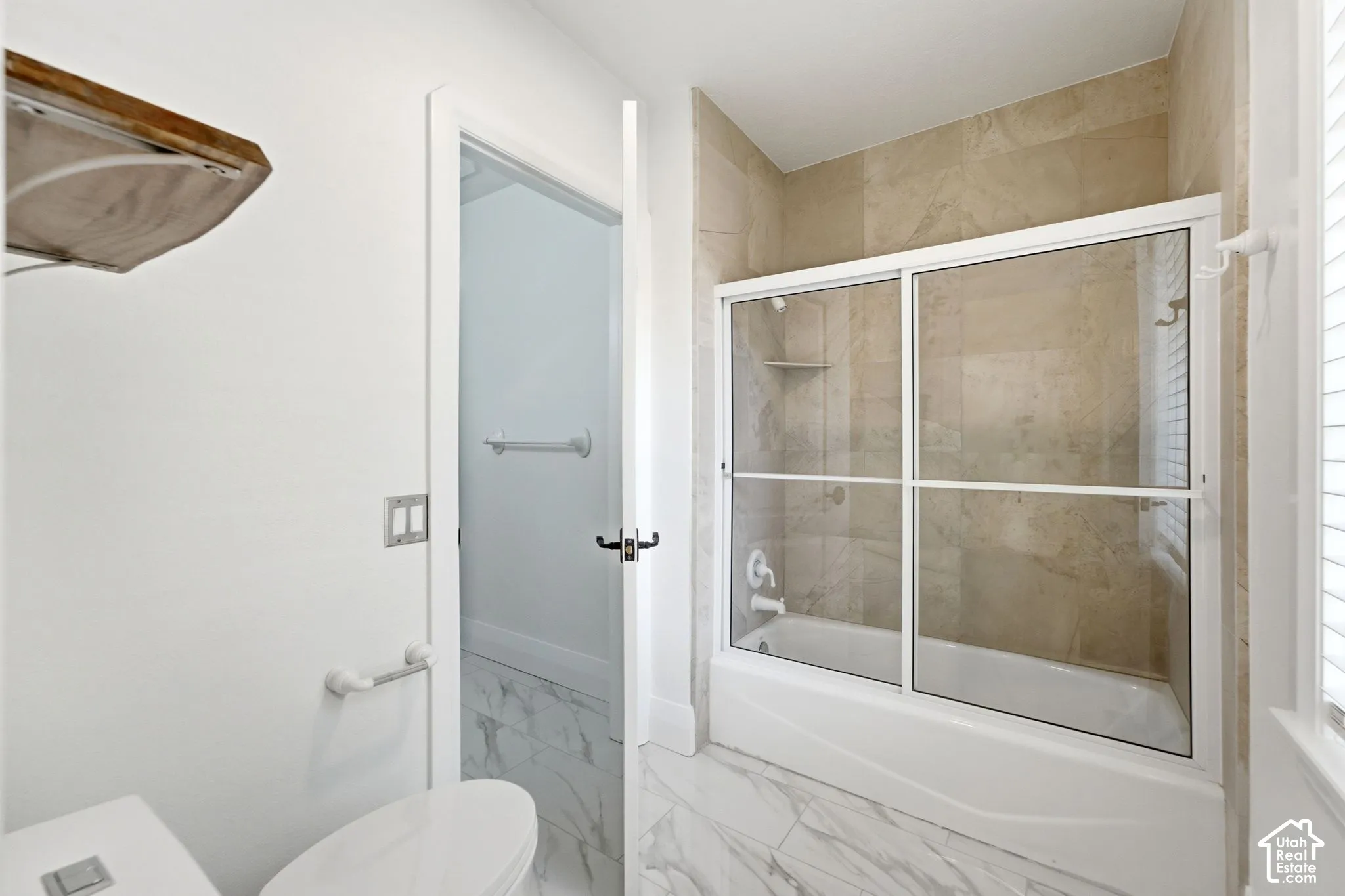 Bathtub with sliding glass enclosure, floor-to-ceiling tile surround, and built-in shower niche