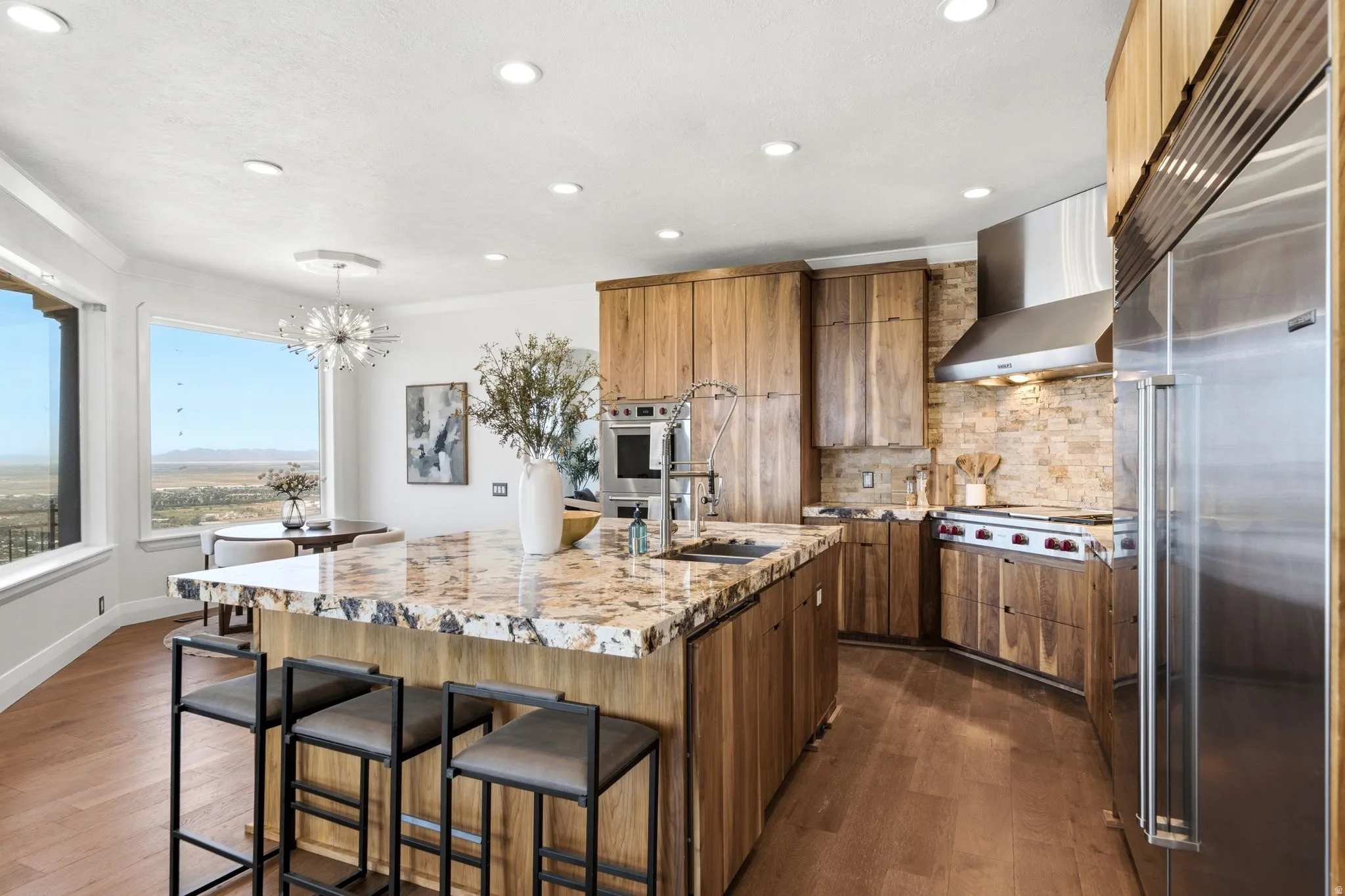 Spacious kitchen featuring an expansive island with a polished countertop, wood-finish cabinetry, stainless steel appliances, and a stone-tiled backsplash