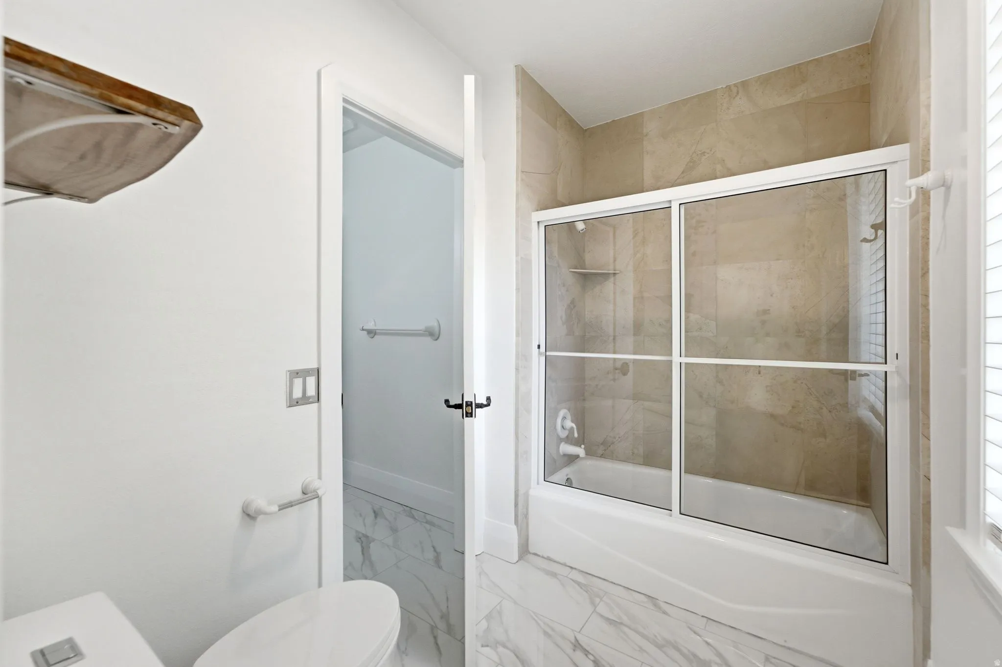 Bathtub with sliding glass enclosure, floor-to-ceiling tile surround, and built-in shower niche