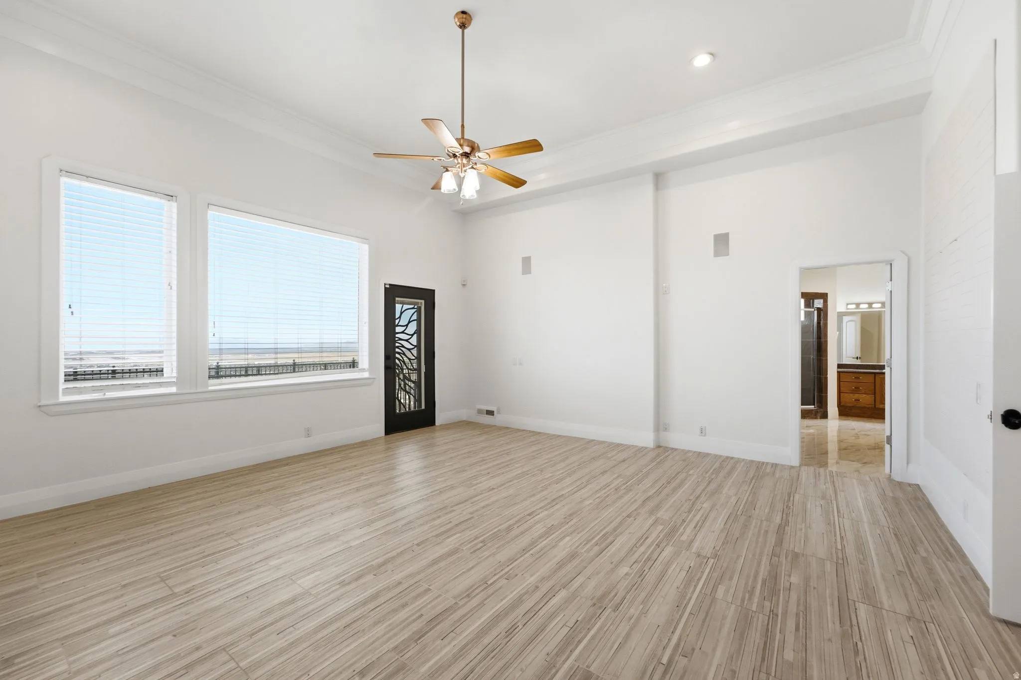 High ceilings with crown molding, light wood-finish flooring, large windows, ceiling fan with integrated lighting, and a decorative frosted glass door