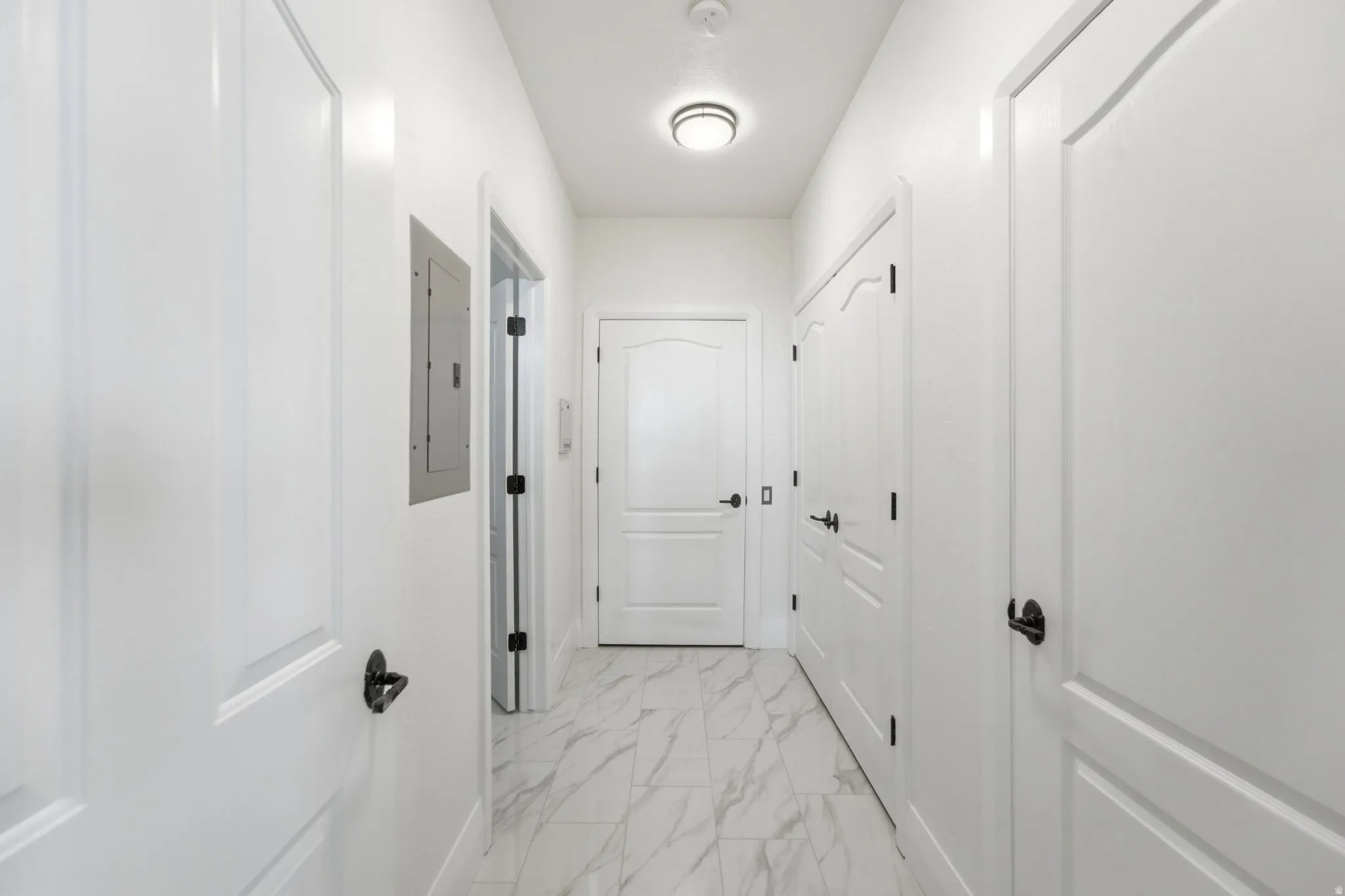 Hallway featuring white panel doors, matte black hardware, recessed lighting, and marble-look tile flooring