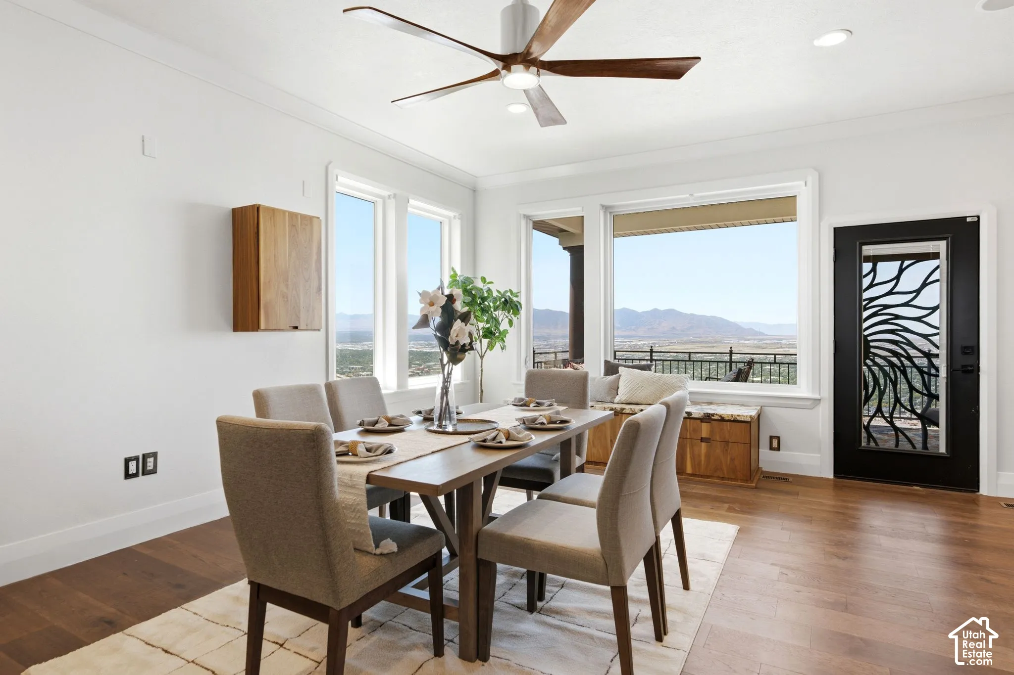 Hardwood flooring, white crown molding, large picture windows, wood-finish wall cabinet, and a decorative glass-paneled door