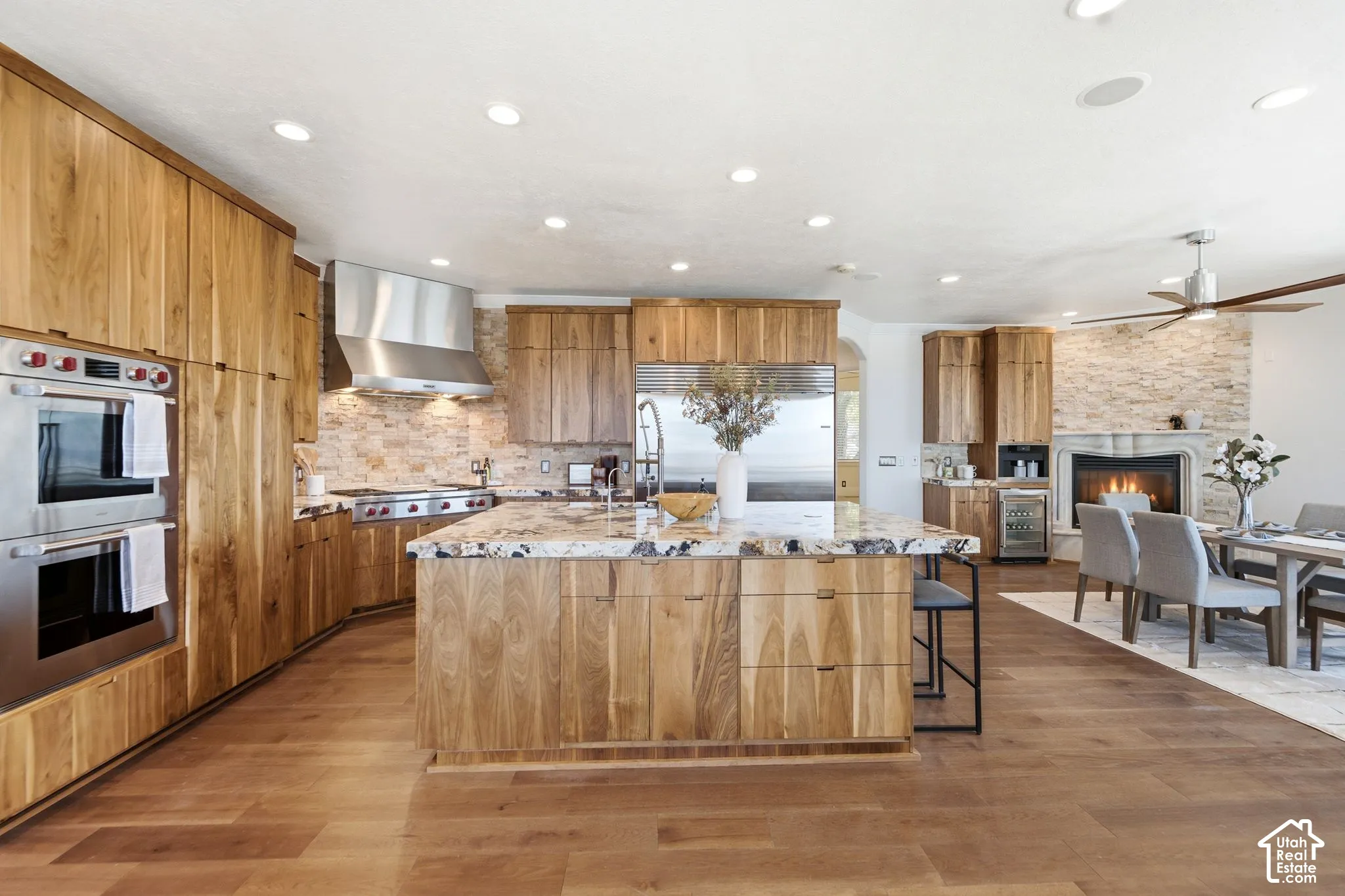 Gourmet kitchen with double wall ovens, wood cabinetry, stone backsplash, and a multi-level island with a built-in sink