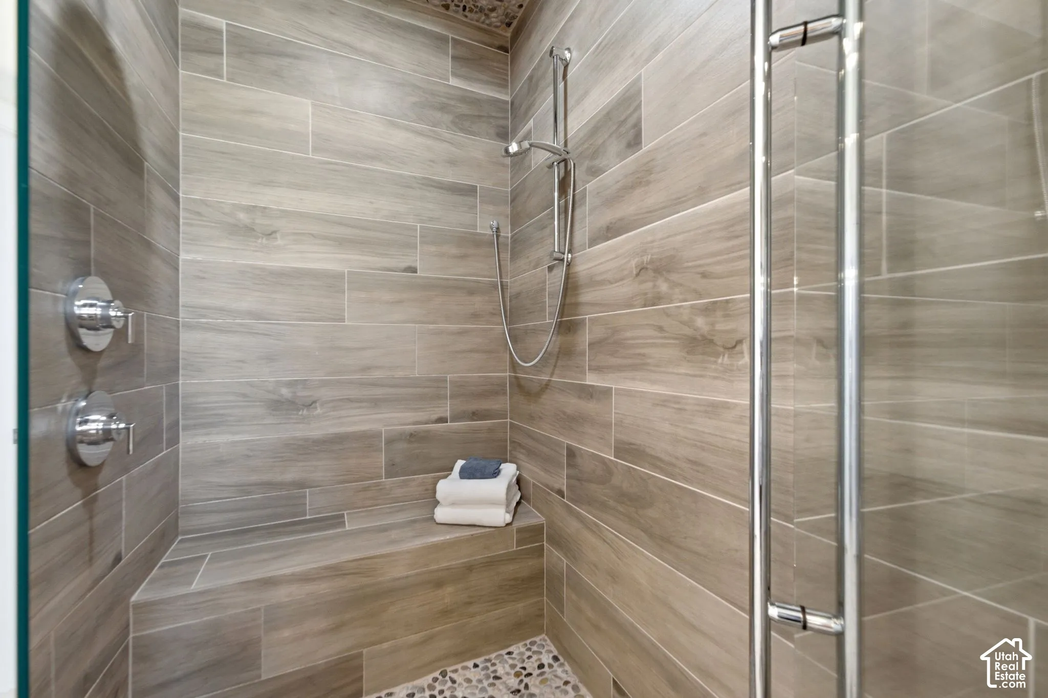 Enclosed shower featuring wood-look tile walls, a built-in bench, a handheld shower fixture, and a mosaic pebble floor