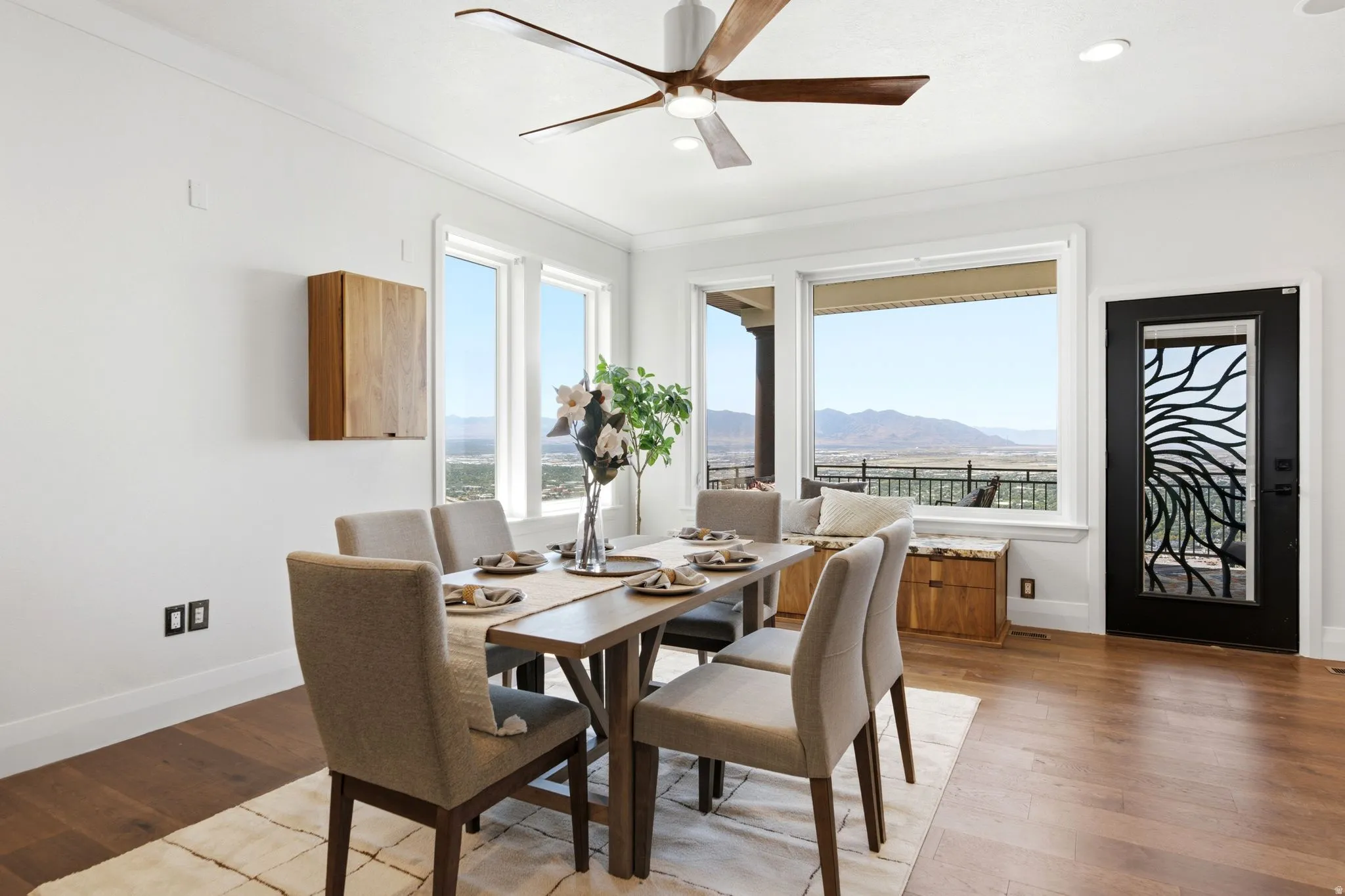 Hardwood flooring, white crown molding, large picture windows, wood-finish wall cabinet, and a decorative glass-paneled door