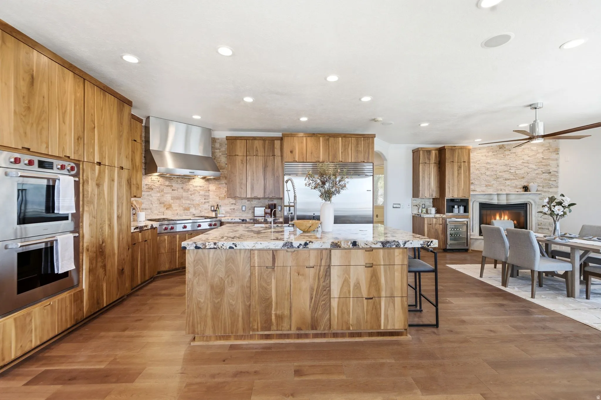 Gourmet kitchen with double wall ovens, wood cabinetry, stone backsplash, and a multi-level island with a built-in sink