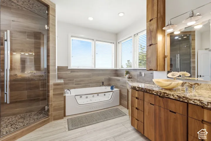 Glass-enclosed shower with tiled walls and pebble floor, soaking tub, wood-finish vanity with stone countertop, and vessel sink