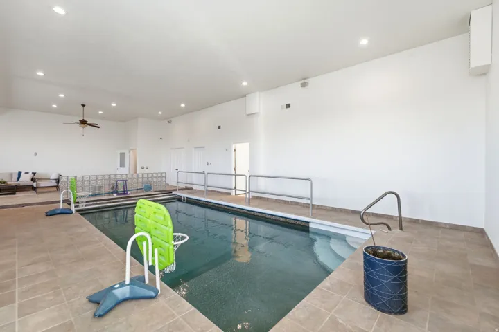 Indoor swimming pool featuring a tiled surround, integrated steps, and handrails