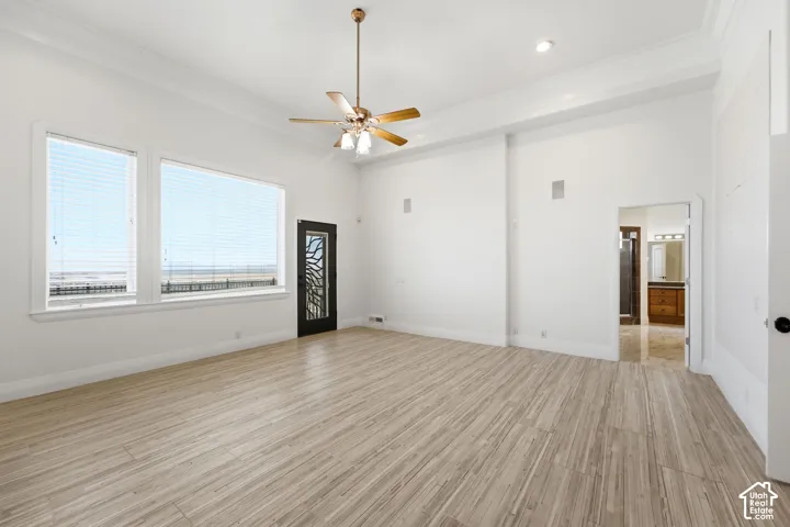 High ceilings with crown molding, light wood-finish flooring, large windows, ceiling fan with integrated lighting, and a decorative frosted glass door