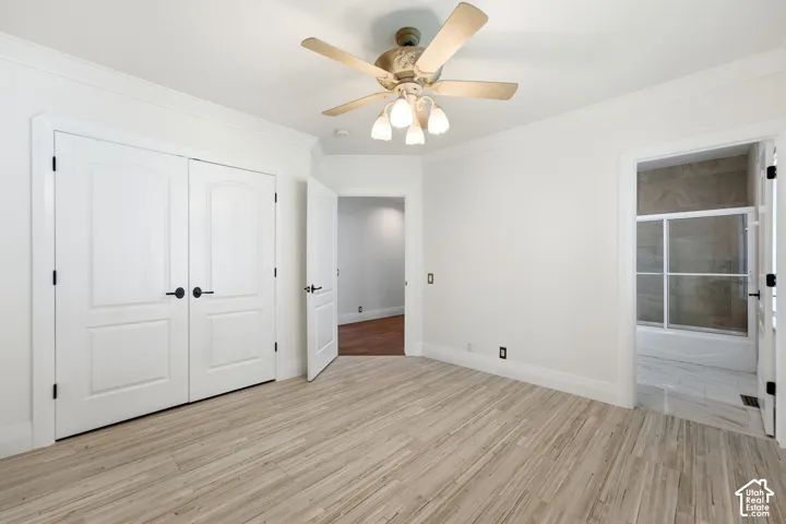 Wood-finish flooring, ceiling fan with light fixture, double panel doors with matte black hardware, crown molding, and an attached bathroom with a shower-tub combination