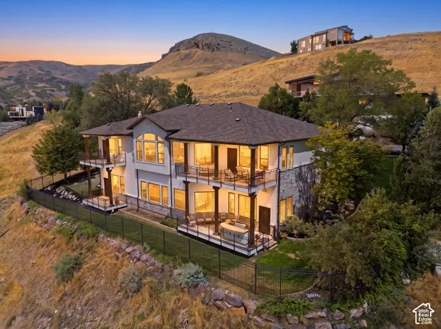 Multi-level residence featuring extensive outdoor balconies, a stucco and stone exterior, large windows, and a dark shingle roof