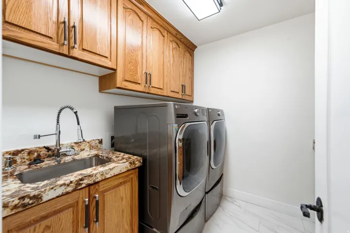 Laundry area featuring wood cabinetry, stainless steel sink, patterned countertop, and white tile flooring