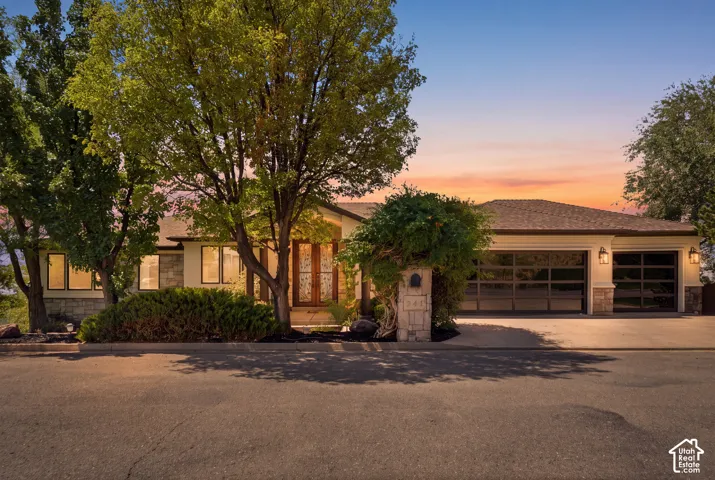 Stone veneer accents on the facade, dual transparent panel garage doors, integrated exterior lighting, a prominent stone mailbox pillar, and established landscaping