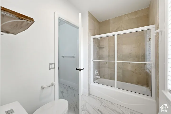 Bathtub with sliding glass enclosure, floor-to-ceiling tile surround, and built-in shower niche