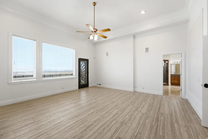 High ceilings with crown molding, light wood-finish flooring, large windows, ceiling fan with integrated lighting, and a decorative frosted glass door