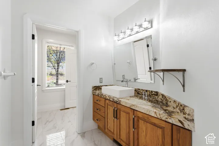 White tile flooring, wood-finish vanity with drawer storage, vessel sink, and a stone-finish countertop