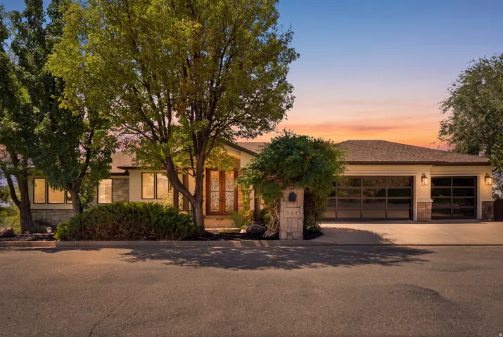 Stone veneer accents on the facade, dual transparent panel garage doors, integrated exterior lighting, a prominent stone mailbox pillar, and established landscaping