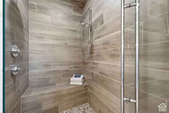 Enclosed shower featuring wood-look tile walls, a built-in bench, a handheld shower fixture, and a mosaic pebble floor