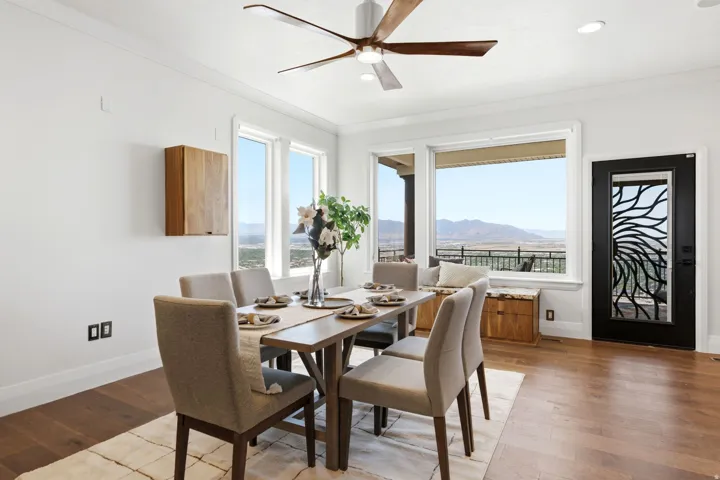 Hardwood flooring, white crown molding, large picture windows, wood-finish wall cabinet, and a decorative glass-paneled door