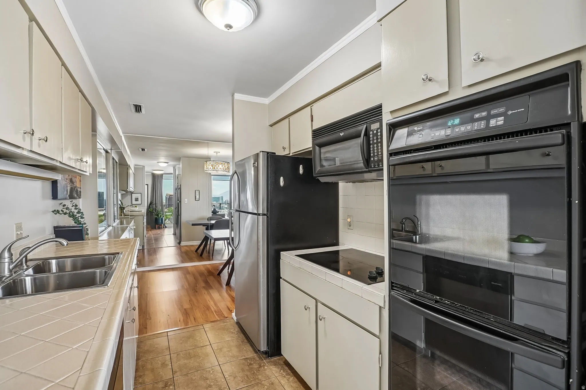 Galley kitchen featuring a dual basin stainless steel sink, built-in microwave, integrated wall oven, and ceramic tile countertops