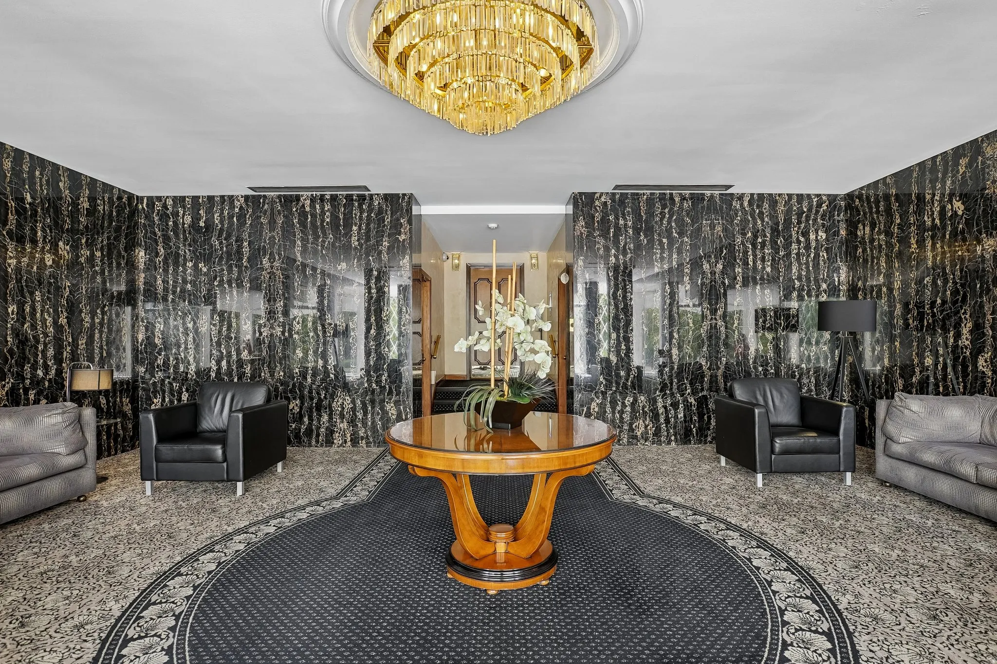 Grand entry featuring a tiered crystal chandelier, polished black and gold veined accent walls, and a round area rug with a decorative border
