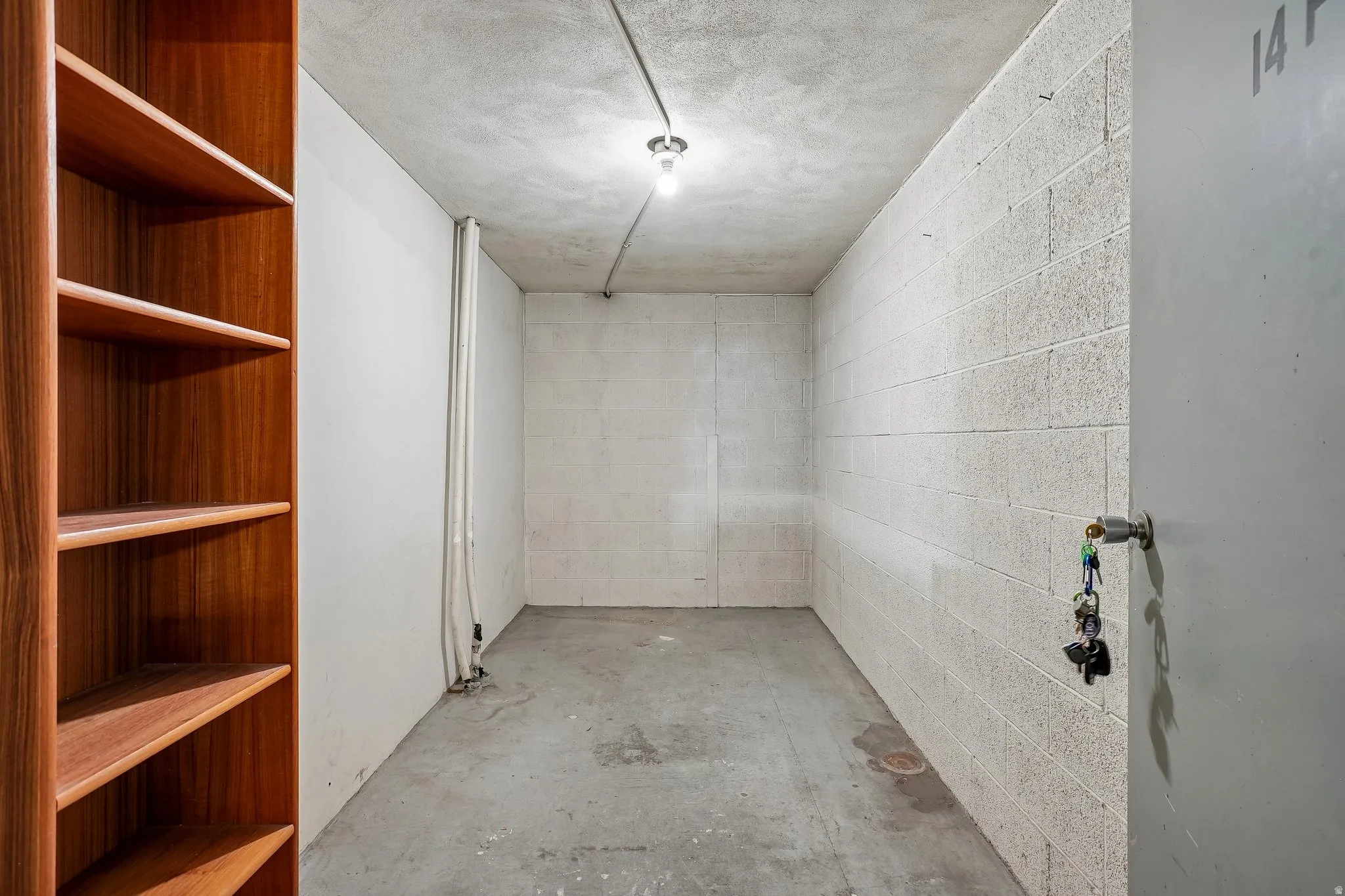 Wood-finish shelving with multiple open shelves, concrete flooring, concrete block wall, and exposed conduit lighting