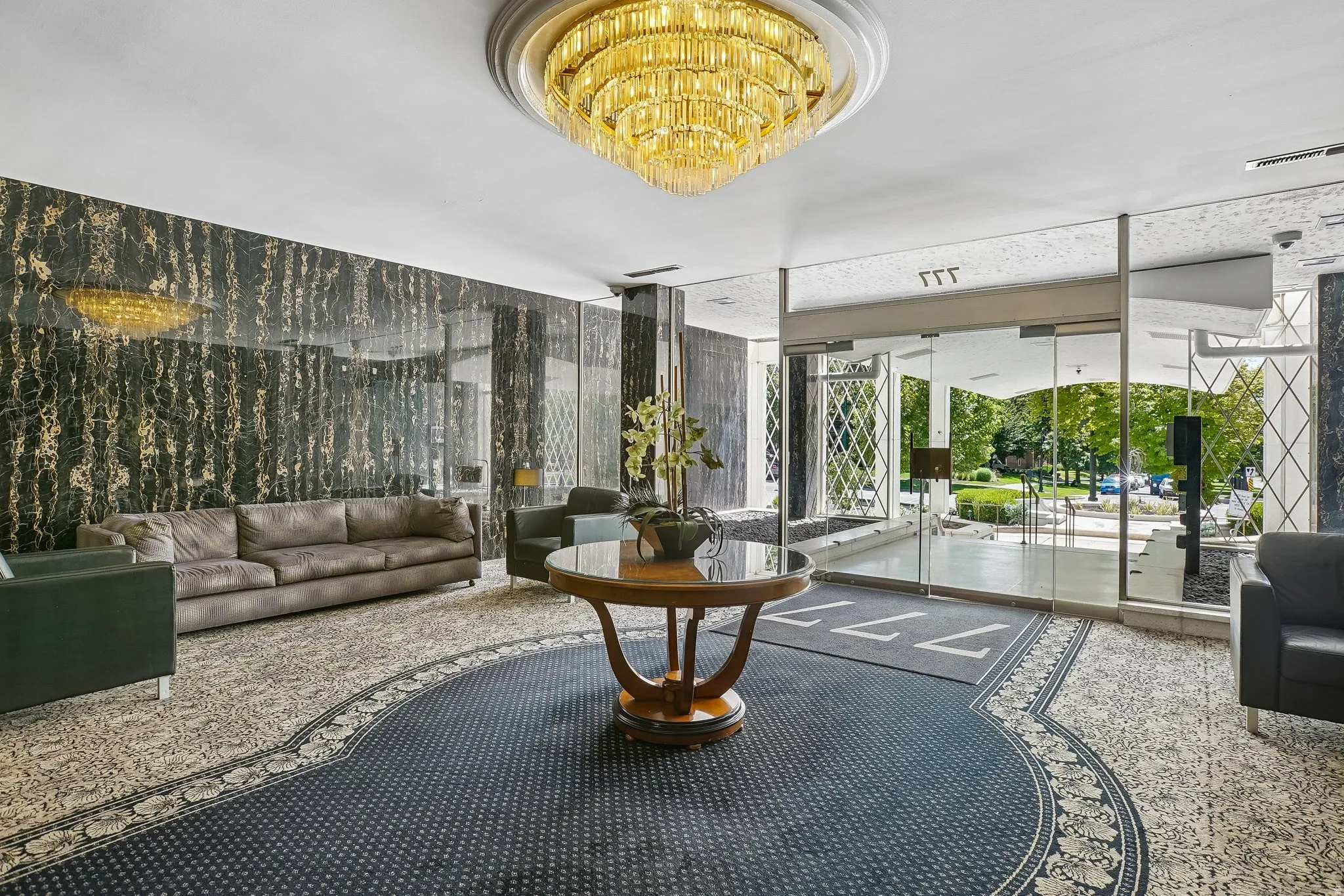 Spacious lobby featuring a large chandelier, patterned carpeting, dark stone-finish accent walls, and glass entry doors