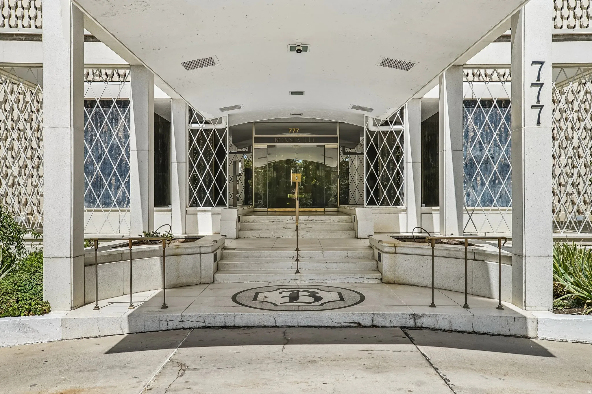 Covered entry with white columns and steps, featuring decorative window grilles and a mosaic emblem
