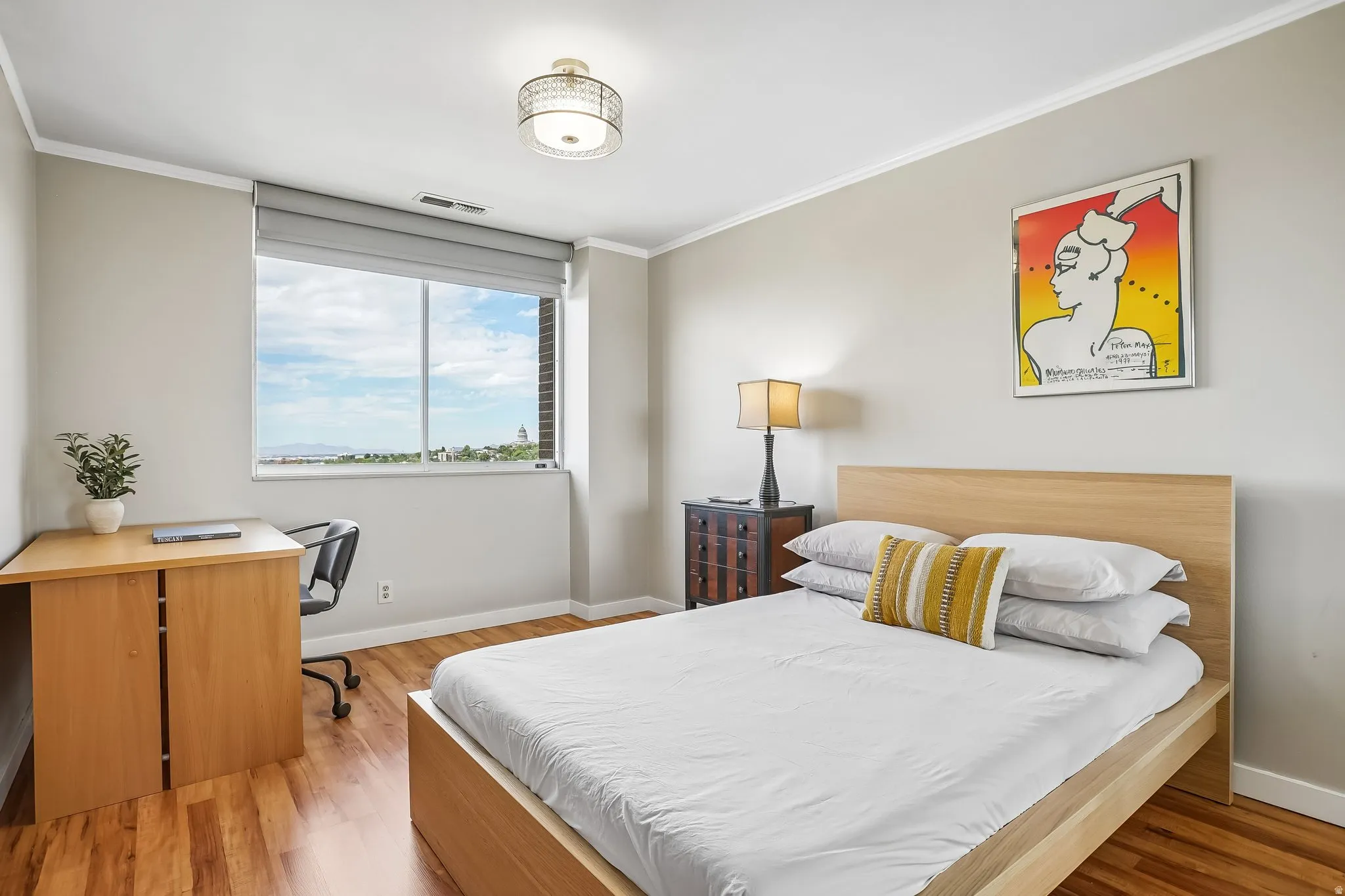 Wood-finish flooring, ceiling-mounted light fixture, window with roller shade, and crown molding