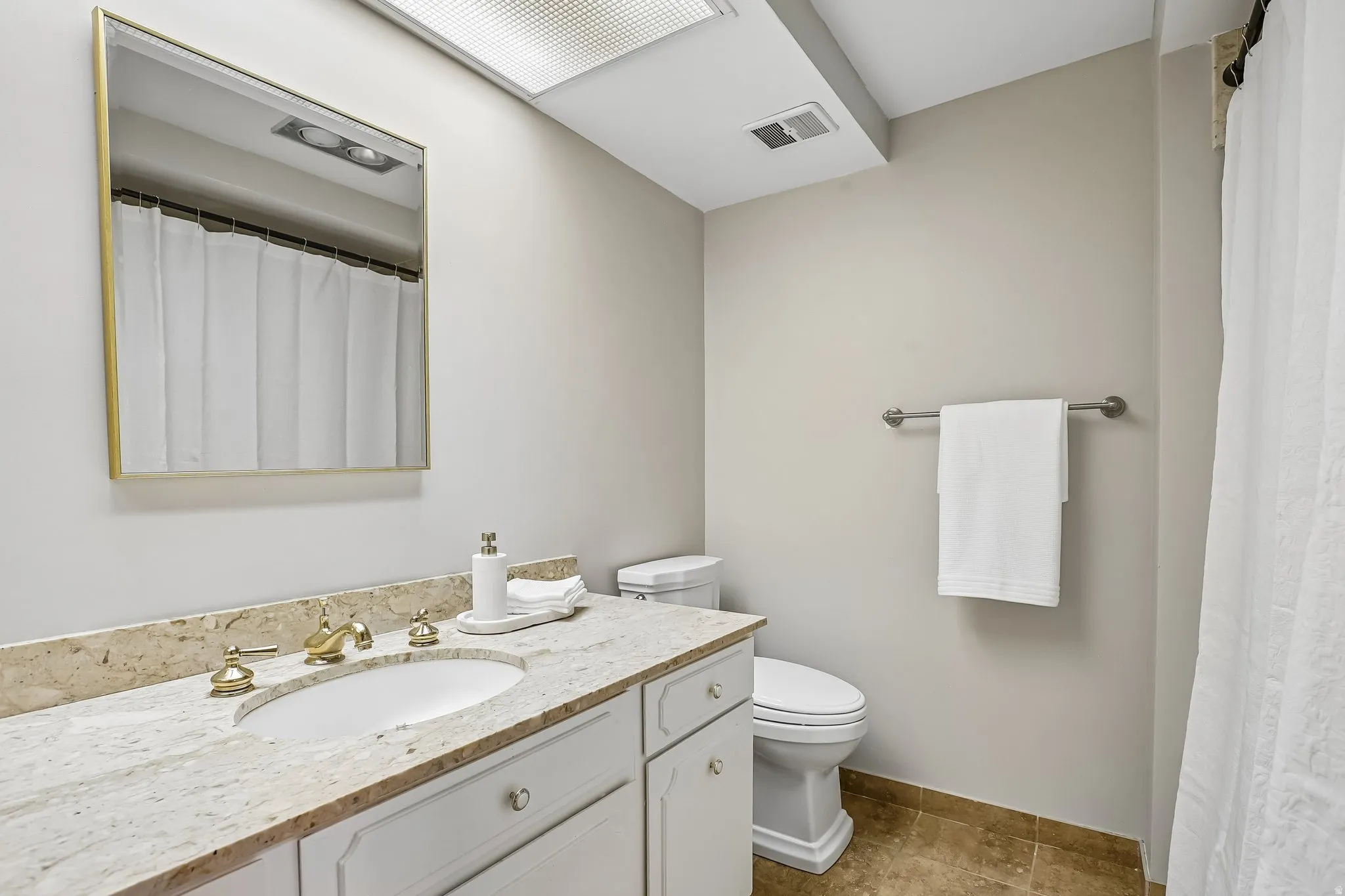 Bathroom featuring a vanity with an undermount sink, a light-toned stone countertop, white cabinetry, and gold-finish fixtures