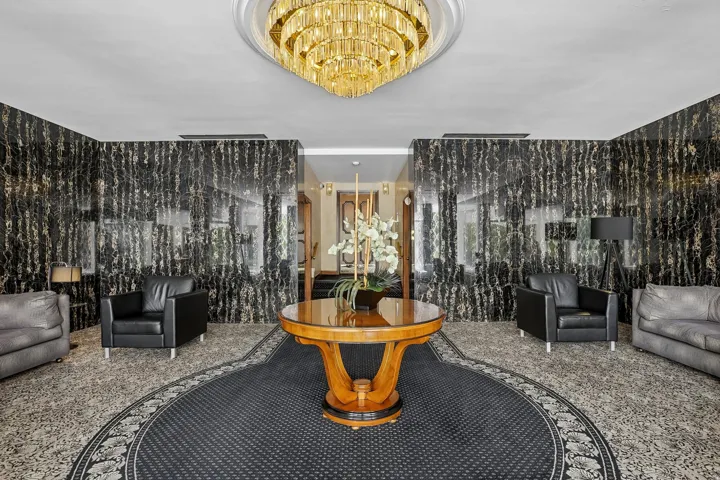 Grand entry featuring a tiered crystal chandelier, polished black and gold veined accent walls, and a round area rug with a decorative border
