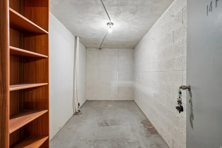Wood-finish shelving with multiple open shelves, concrete flooring, concrete block wall, and exposed conduit lighting