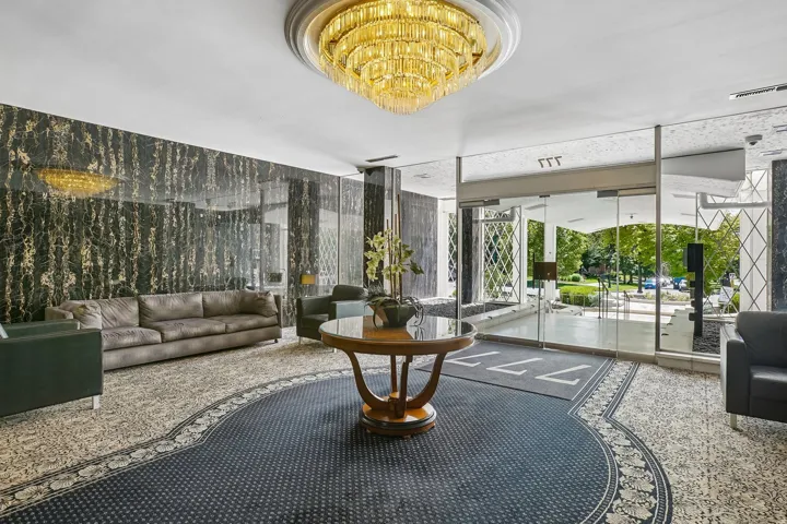 Spacious lobby featuring a large chandelier, patterned carpeting, dark stone-finish accent walls, and glass entry doors