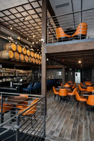 Multi-level interior featuring wood-finish flooring, exposed ceiling grid with pendant lighting, a built-in bar, and metal railing