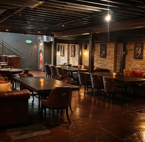 Exposed ceiling joists with track lighting, brick wall accents, dark-stained concrete flooring, and an industrial-style staircase with metal railings
