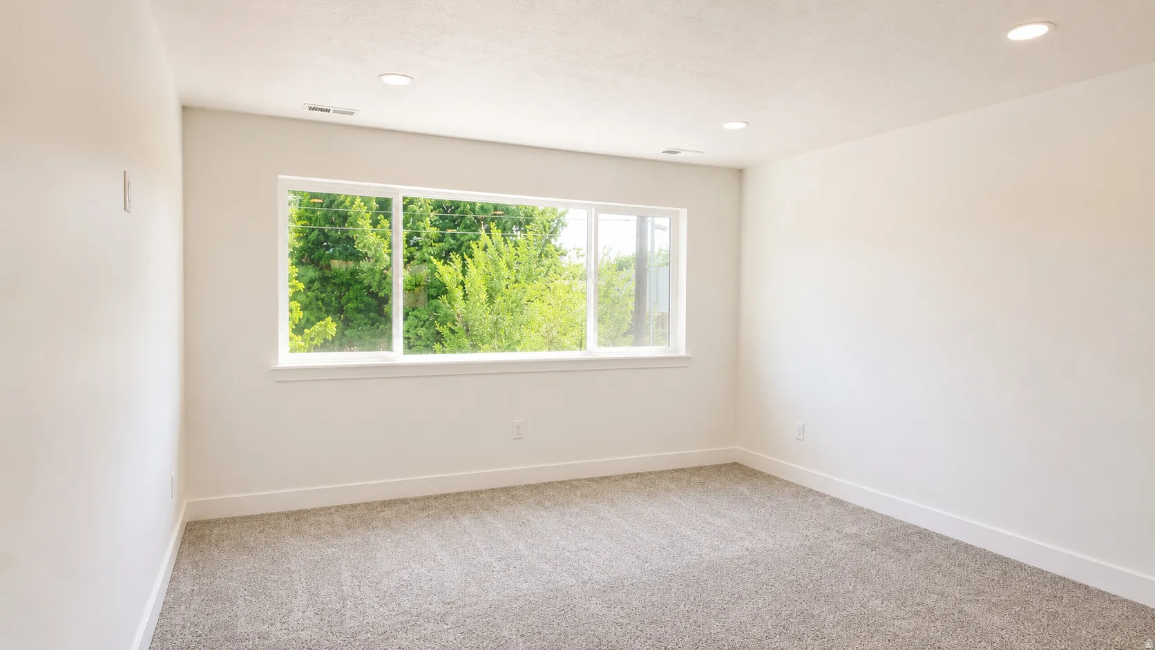 Recessed lighting, plush carpet flooring, and a large window with white trim