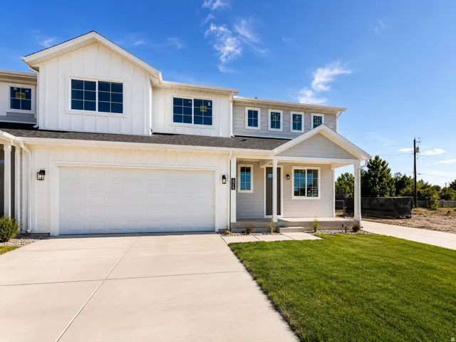 White exterior siding, attached two-car garage, covered front porch, concrete driveway, and a manicured lawn