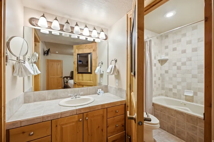 Wood-finish vanity with an integrated sink, tile countertop, and a multi-bulb light fixture