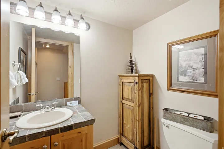 Light wood-finish vanity with a tile countertop, integrated sink, and an overhead vanity light fixture