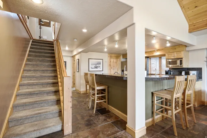 Staircase with carpeted treads and wood handrails, slate-style flooring, kitchen with light wood cabinetry, built-in microwave, and track lighting