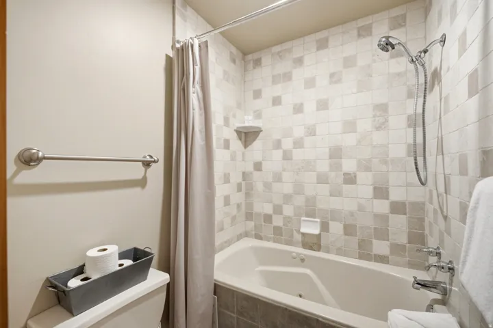 Bathtub with tiled surround, handheld shower fixture, and a coordinated shower curtain