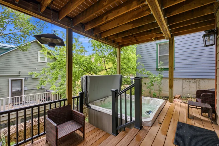 Wood-finish deck with a built-in hot tub, black railing, and an overhead heater