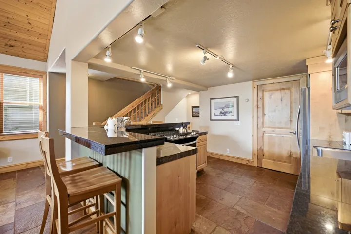 Kitchen featuring dark stone countertops, wood-finish cabinetry, stainless steel appliances, and slate-finish flooring