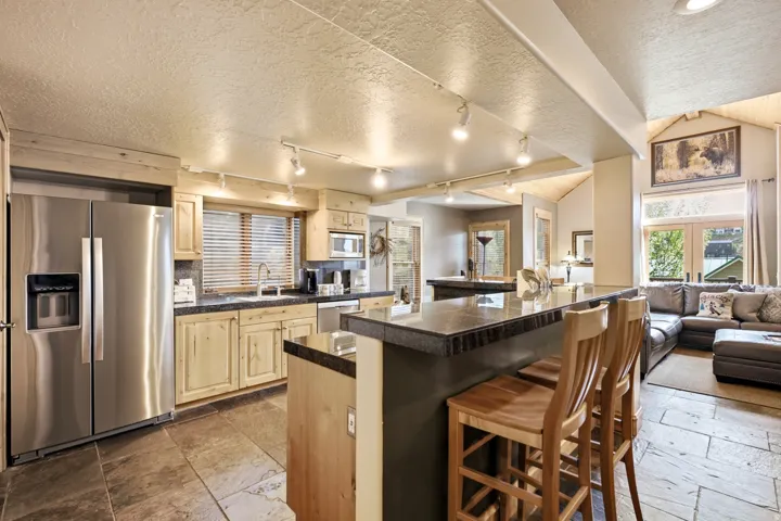 Kitchen featuring stainless steel appliances, wood cabinetry, a center island with bar seating, and stone tile flooring