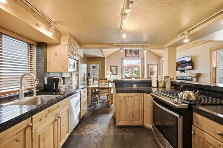 Kitchen featuring wood cabinetry, dark countertops, a stainless steel sink, a stainless steel dishwasher, and a built-in microwave
