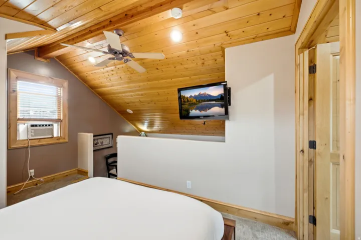 Wood-paneled sloped ceilings, wood-finish window trim, ceiling fan, and solid wood door