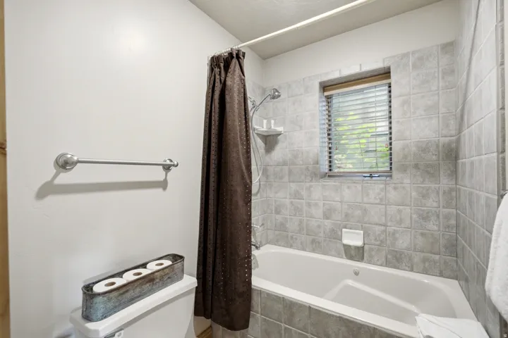 Bathtub with tiled surround, shower fixture, and a window with blinds